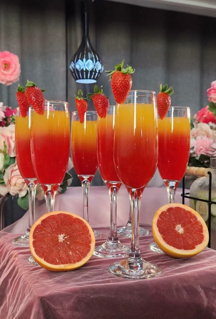 Strawberry-garnished sunrise drinks in champagne flutes