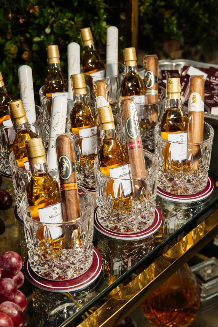 Miniature whiskey bottles and cigars presented in cut-glass tumblers for cocktail hour