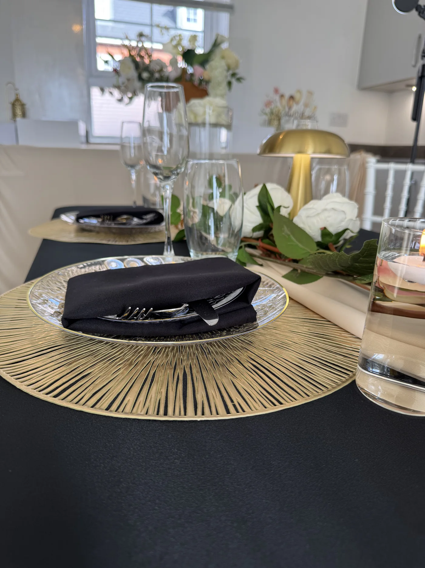 A black and gold place setting with a black napkin, gold charger and glassware