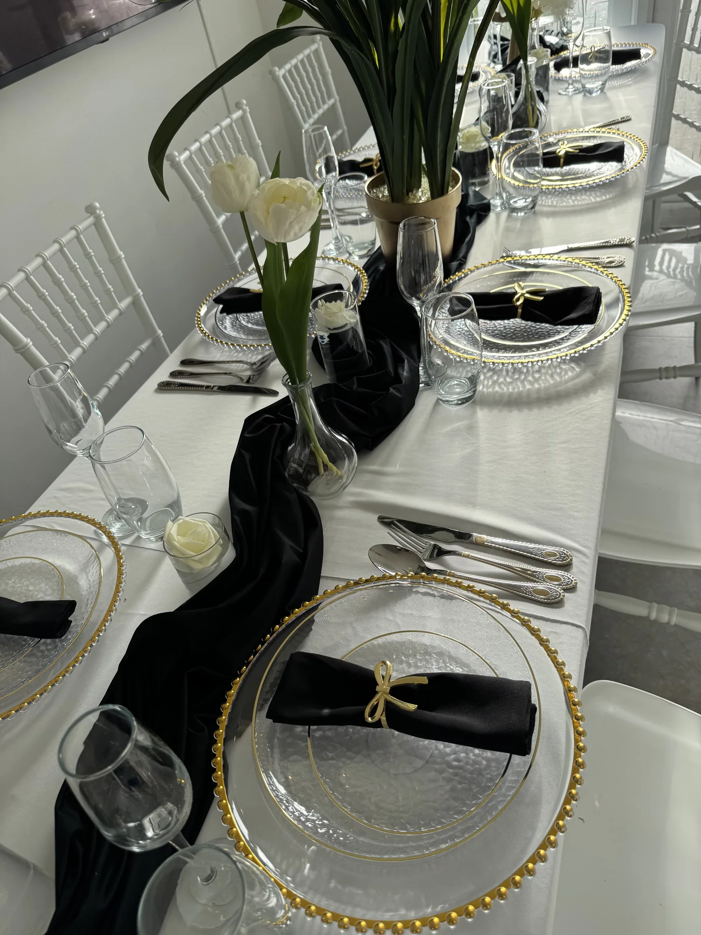 A long table styled with white linen, black runners, gold chargers and white tulips