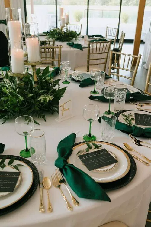 An emerald green and gold wedding table detail with green napkins, glassware and candles