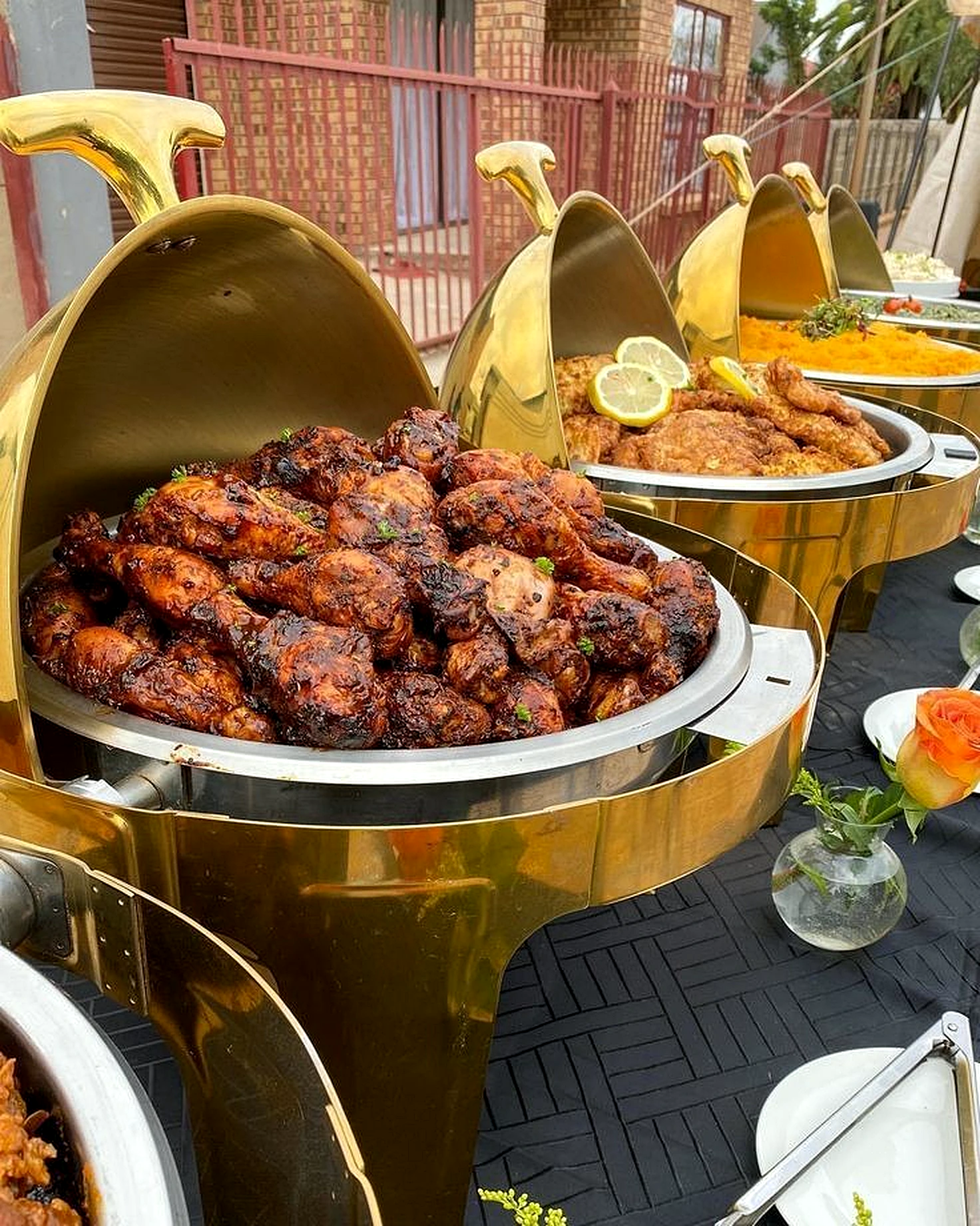 Golden chafing dishes filled with grilled chicken, rice and celebration dishes